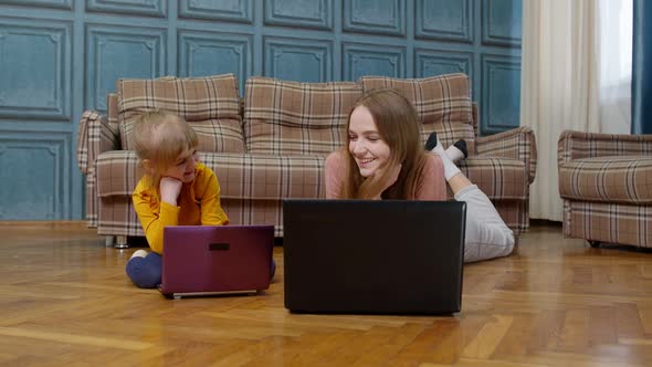 Woman Nanny and Child Girl Studying Together with Computer Laptop While Lying on Warm Floor at Home