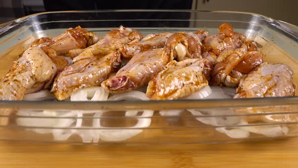 The marinated chicken wings are laid out on the onion rings in a glass baking dish.