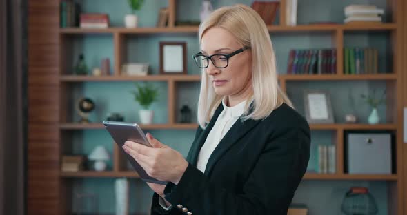 Business Lady in Formal Wear in Glasses Uses Tablet pc and Looking Into Camera in Modern Office