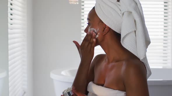 African american woman applying face mask looking in the mirror at bathroom