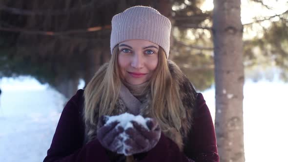 A Beautiful Girl Enjoys Nature and Blows Snow From Her Hands