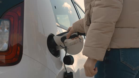 Close Up Womans Hand Inserts an Electric Plug Into the Car to Charge at Sunny Day