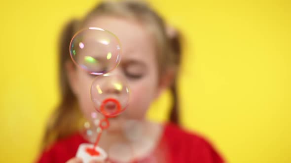 Closeup of Playful Charming Girl Blowing Soap Bubbles at Yellow Background