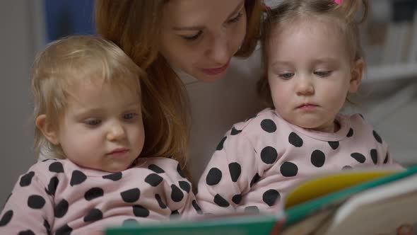 Closeup of Baby Twin Sisters Listening to Mother Reading Book in the Evening