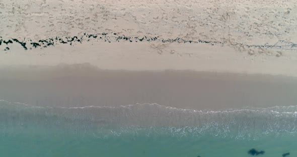 Static top down view of tropical beach, foamy ocean waves washing sand. Waves hitting sand beach