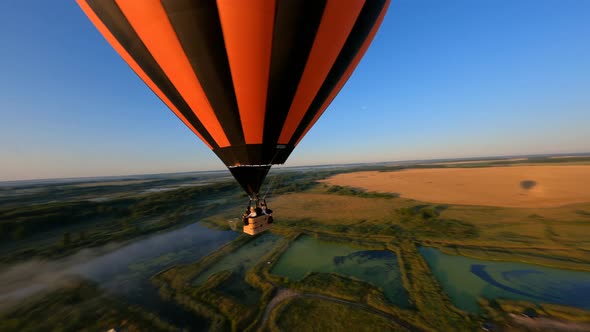 Drone flying close to black and orange hot air balloon floating above lake