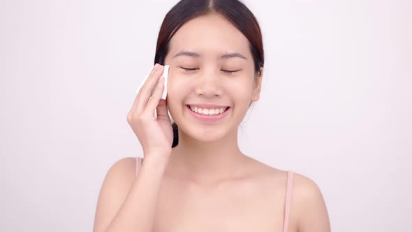 Happy Asian girl using cotton pad applying facial wipe on her face, removing makeup.