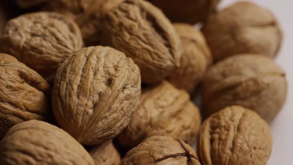 Cinematic, rotating shot of walnuts in their shells on a white surface 