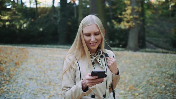 Young Blonde Girl Walking in Autumn Park and Throwing Golden Leaves in the Air, Slow Motion