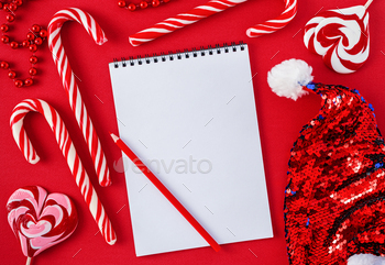 White wish list blank with candies and Santa hat on red background.