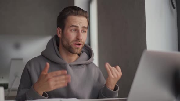 Serious man in hoodie talking by video call on laptop and counting on fingers