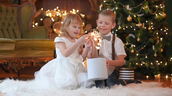 Happy little children sitting on the floor near the Christmas tree opens gifts.