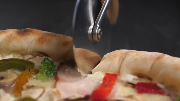 A Pizza Knife Rolls Over the Surface of a Fresh Pizza Cutting It
