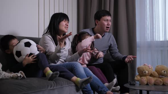 Asian Family Watching Soccer Game in Domestic Room