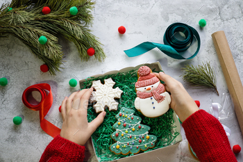 Girl's hands in red knitted sweater put gingerbread in the form of snowman into gift box 