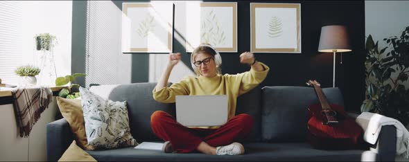 Woman in Headphones Listening to Music on Laptop at Home