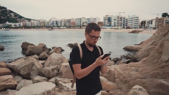 Man Is Viewing Pictures, Reading Messages in Phone, Stands Against Bay and City