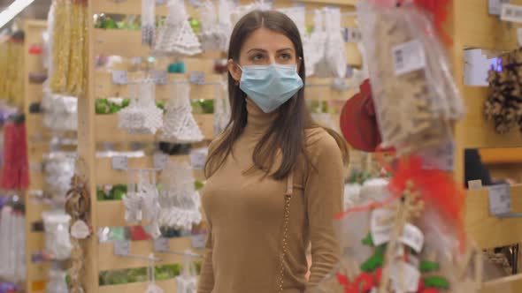 Young Woman in Face Mask Walks Along Store and Looks Around