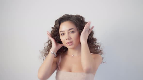 A woman with long curly hair curled on a curling iron demonstrates her hairstyle