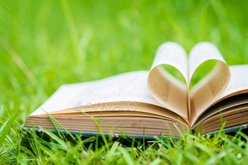 Closeup of an old open book laying on green grass with its pages forming a heart shape