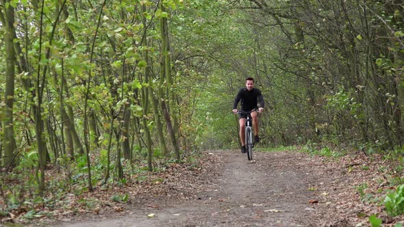 A Cyclist Rides Down a Path Through a Forest - Front View