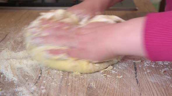 Woman making homemade gnocchi dough on a wooden table at home.