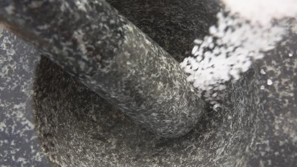 Closeup of a White Sea Salt Falling and Bouncing Into the Grey Stone Mortar