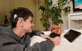 deaf boy with cochlear implant playing computer game on playstation and watching cartoon with dog - PhotoDune Item for Sale