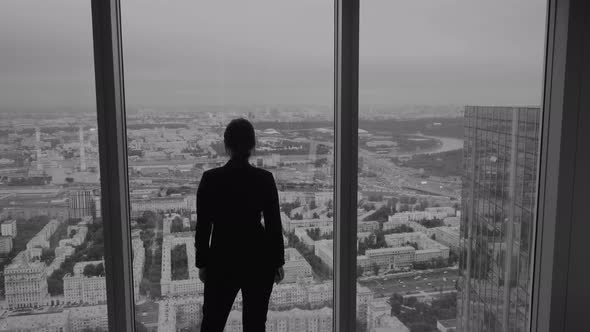 Business Woman Stands Near a Large Window on a High Floor of a Skyscraper