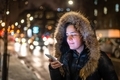 Woman checking her phone standing beside street in a winter evening  - PhotoDune Item for Sale