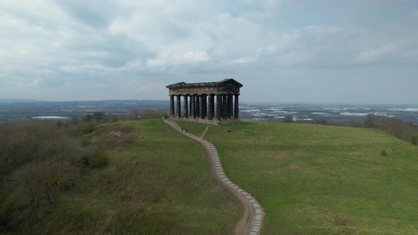 Aerial cinematic rotating shot of Penshaw Monument with grass field and stairs in the foreground.