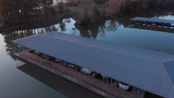 Aerial footage flying over boat docks towards land at sunset with reflections in the calm water