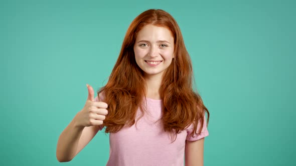 Young Woman Showing Thumb Up Sign Over Blue Background. Positive Young Girl Smiles To Camera. Winner
