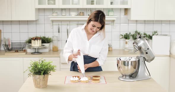 Portrait of a Young Woman Pastry Chef Decorating Biscuit Tartlet with Cream From Pastry Bag