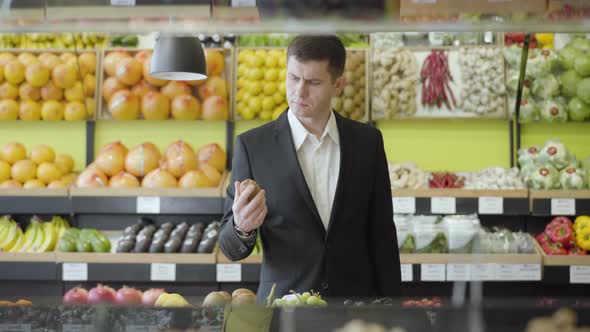 Serious Caucasian Man in Suit Choosing Kiwi Fruit in Grocery. Portrait of Confident Adult