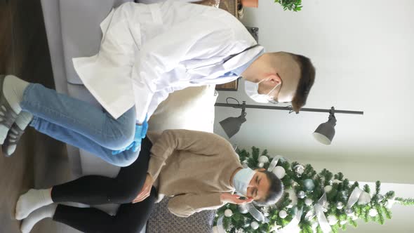 Male doctor in a mask and glasses and a woman in a mask, a sick patient at home, vertical video