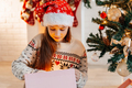 Girl in a red Santa hat opens a gift at home in the living room - PhotoDune Item for Sale