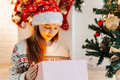 Girl in a red Santa hat opens a gift at home in the living room - PhotoDune Item for Sale