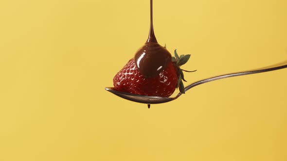 Fresh Strawberry on Metal Pastry Spoon Covering with Melted Liquid Chocolate on Yellow Background