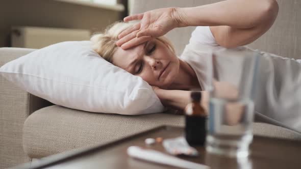 Sick Woman with Headache Resting in Bed with Some Pills From Her Medical Treatment on a Table in the
