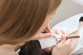 Eyelash extension procedure. Master tweezers fake long lashes beautiful female eyes., back view - PhotoDune Item for Sale