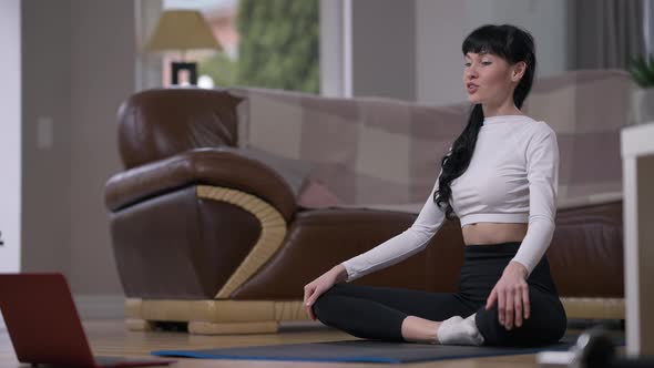 Confident Slim Sportswoman in Lotus Pose Talking in Slow Motion Smiling Sitting with Laptop at Home