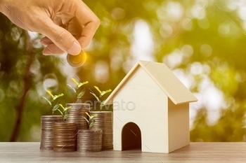 A businessman hand holding coin over growing plant on stacked coins and resident house model on wooden table.