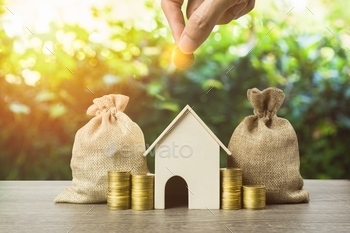 stment for future concept. A man hand putting money coin over small residence house and money bag with nature background. A sustainable investment.