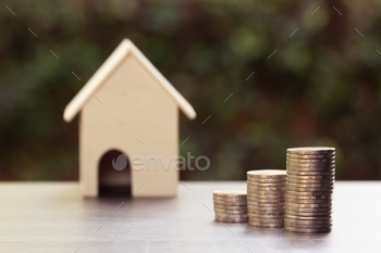 ncept. Stacked coins and blurred house model wooden table with nature background. Depicts  house investment Or real estate that grows continuously.