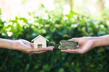 into cash concept : Hand holding home model change to money with green nature as background. Conceptual changing residence into cash.