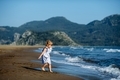 Toodler caucasian blonde girl in blue dress plays on the sandy beach.  - PhotoDune Item for Sale
