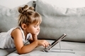 Toddler girl lies on couch at home and playing with digital wireless tablet computer. - PhotoDune Item for Sale