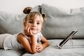 Toddler girl  lies on couch at home and playing with digital wireless tablet computer. - PhotoDune Item for Sale
