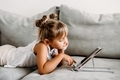 Toddler girl  lies on couch at home and playing with digital wireless tablet  - PhotoDune Item for Sale